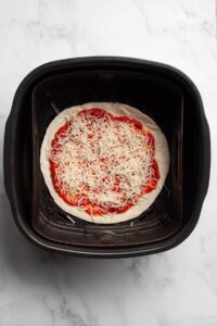 adding shredded mozzarella cheese to the tortilla pizza before air frying